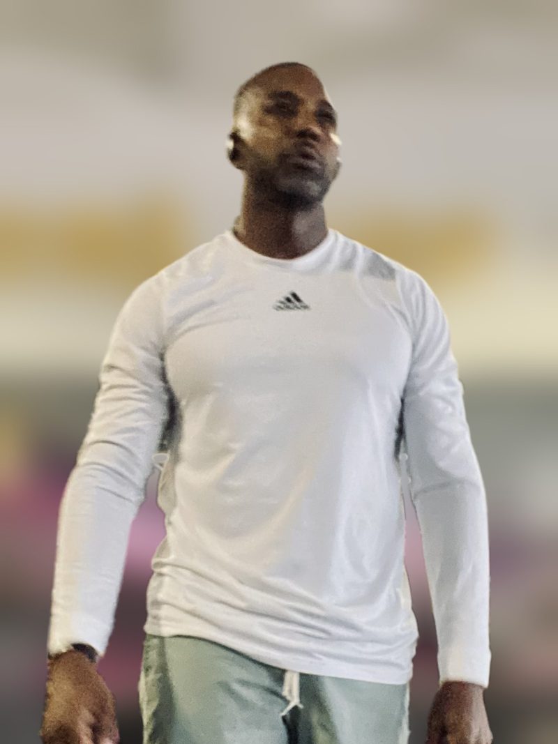 Mike Rumph in a white long-sleeve Adidas shirt and gray shorts walks through a gym, the background softly blurred
