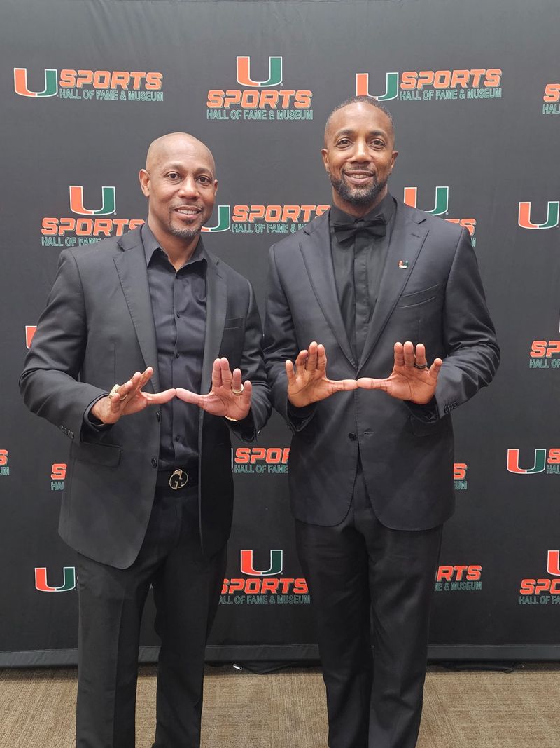 Mike Rumph, right, with two friends in colorful patterned jackets on the field-level sideline at a Hurricanes home game