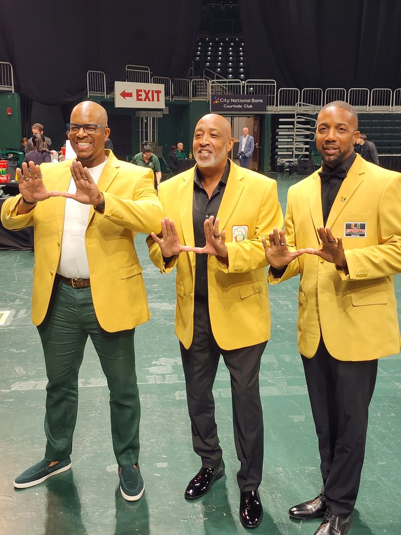 Mike Rumph, right, and two other men in gold Hall of Fame jackets make the U hand sign on the arena floor