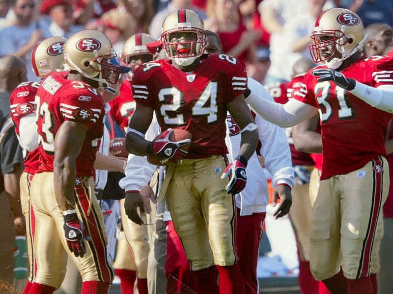 Mike Rumph, number 24 for the San Francisco 49ers, holds the football as teammates gather around him during a game